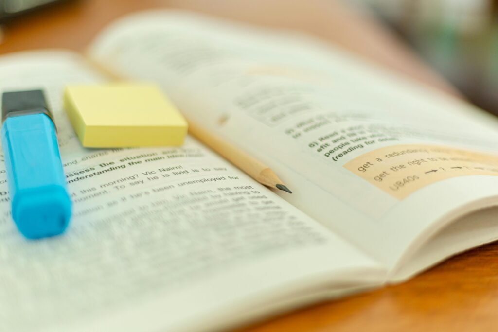 Close-up of an open book with a highlighter and sticky notes for study reference.